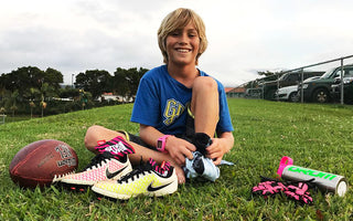 Smiling boy sitting on a grass field with a ball and a pair of Nike Football Shoes with SmellWell inserts in them.