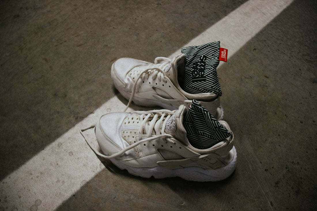 A pair of white sneakers with SmellWell Inserts in them on a cement floor 