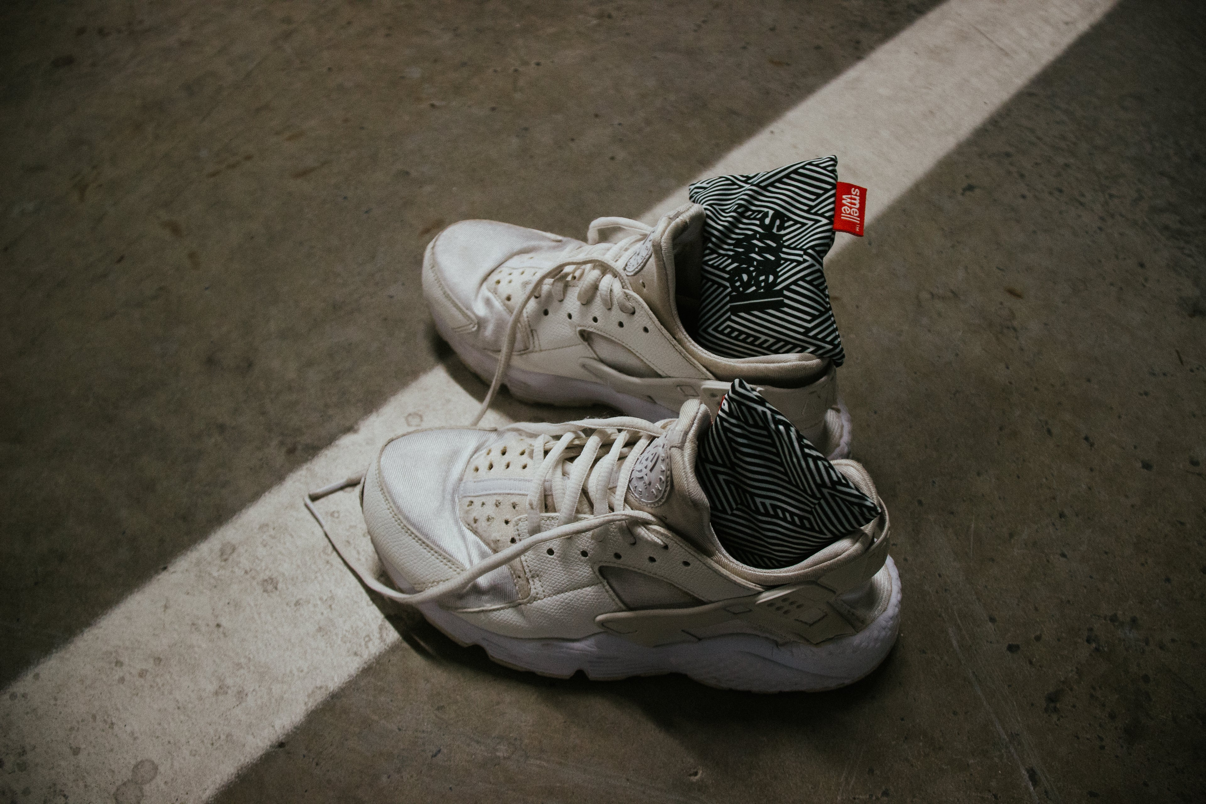 A pair of white sneakers with SmellWell Inserts in them on a cement floor 