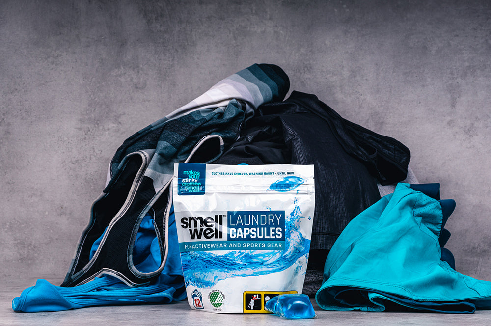 A pack of SmellWell Laundry Capsules in front of a pile of laundry