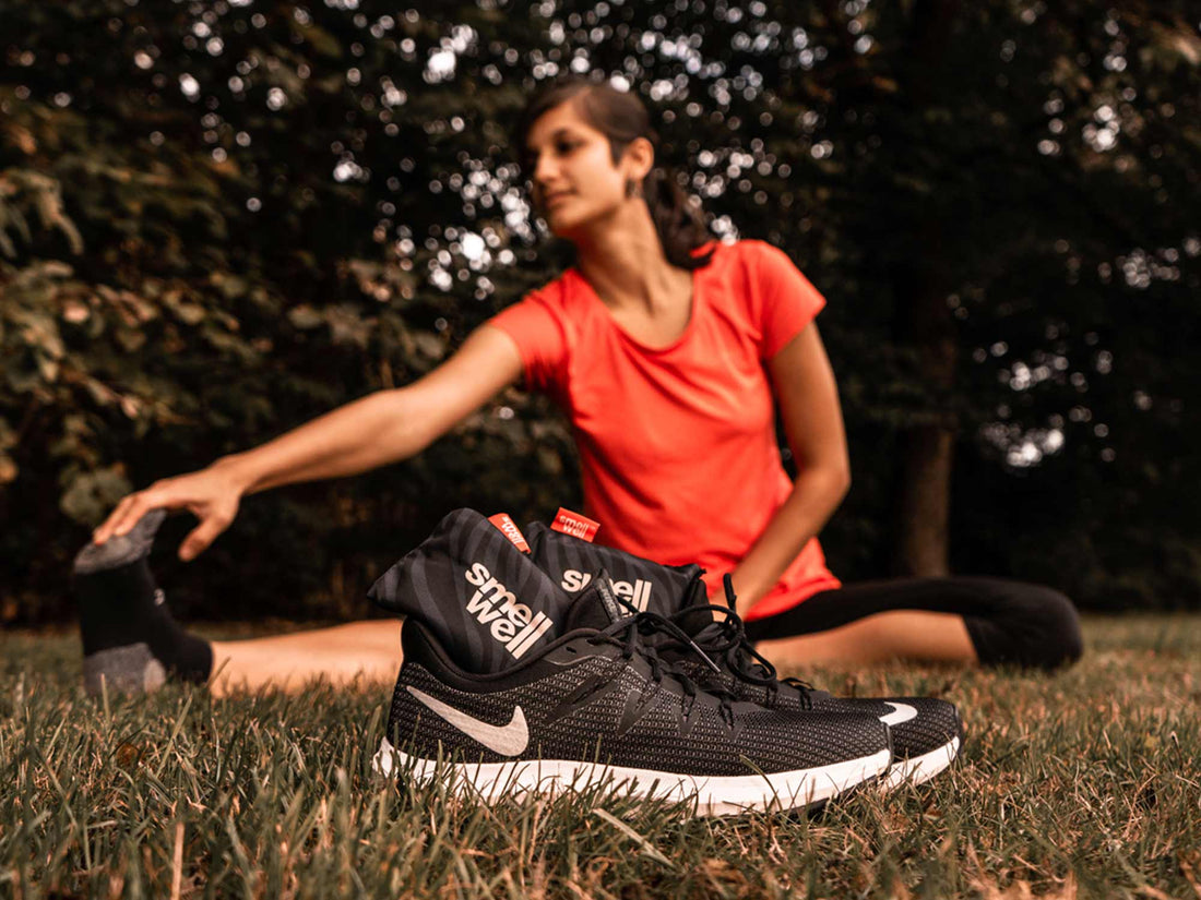 Woman stretching on a grass field behind a pair of Black Nike running shoes with black SmellWell inserts inside them.