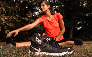 Woman stretching on a grass field behind a pair of Black Nike running shoes with black SmellWell inserts inside them.