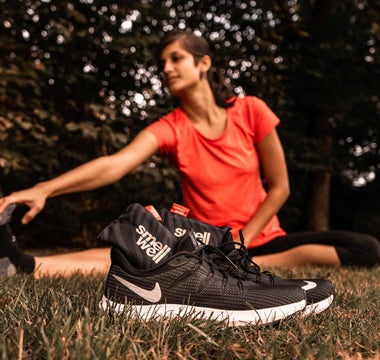 Woman stretching on a grass field behind a pair of Black Nike running shoes with black SmellWell inserts inside them.