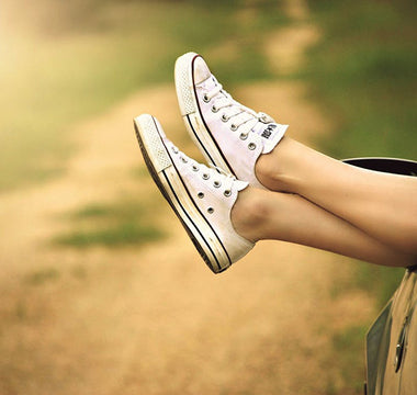 A pair of legs, with feet wearing white Converse sneakers, sticking out relaxed from a car window in summer time