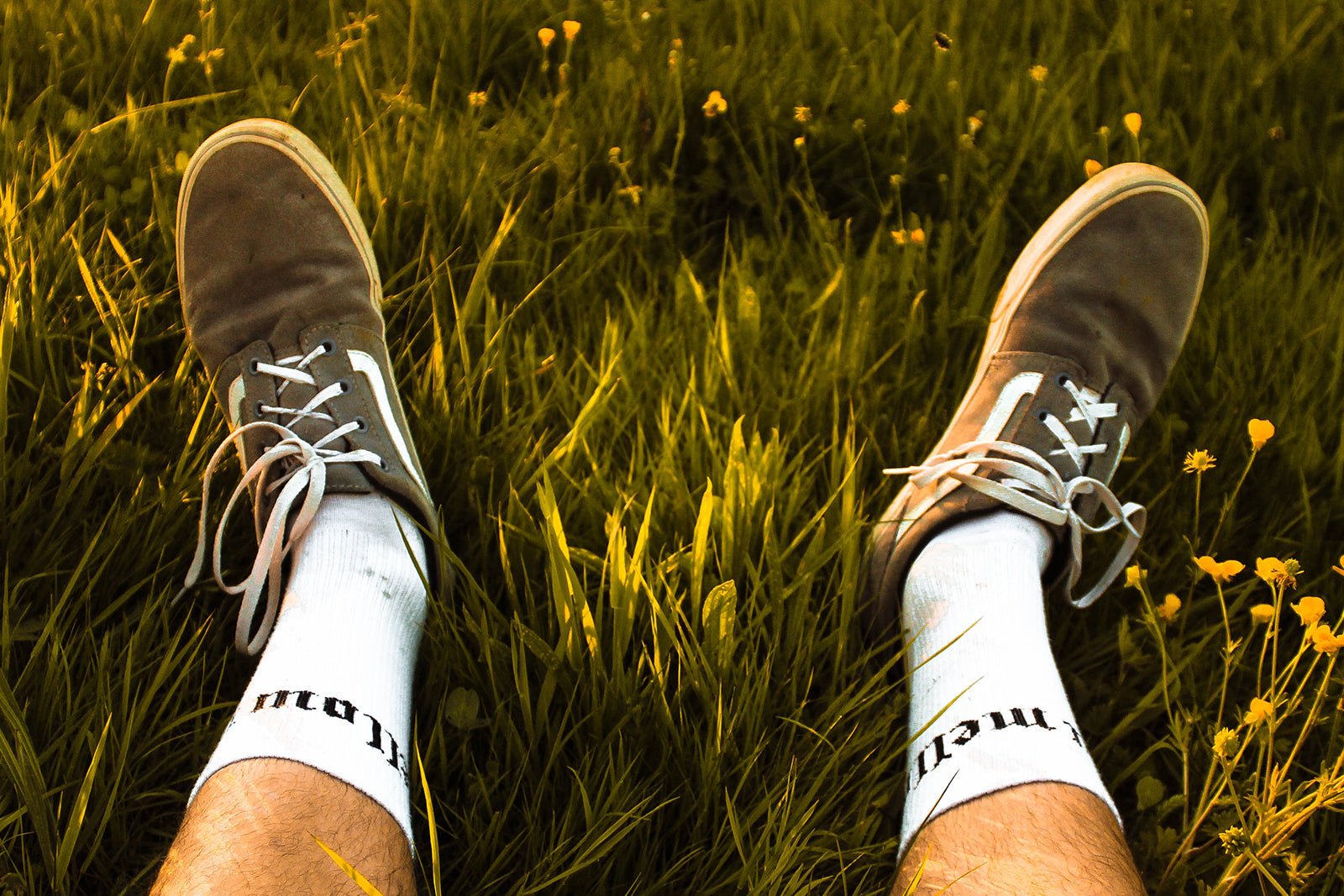Selfshot image of a mans feet in green grass with yellow flowers