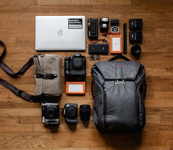 Tophead view of a backpack. Different accessories, such as a laptop and a camera, spread out in a organized grid around it.