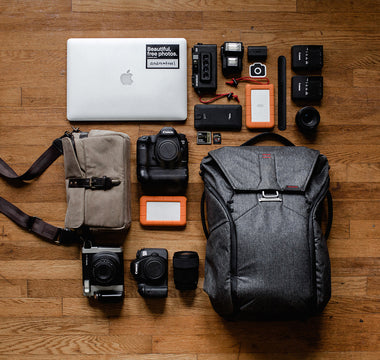 Tophead view of a backpack. Different accessories, such as a laptop and a camera, spread out in a organized grid around it.